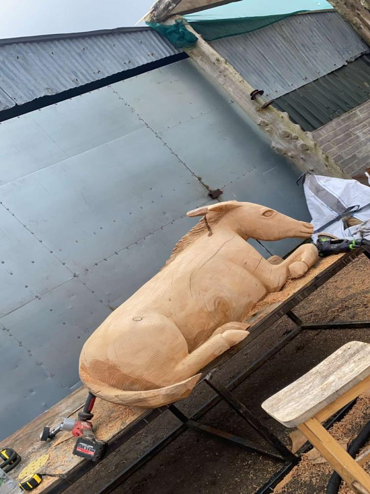 A large, intricately carved wooden bull sculpture in progress at a sawmill, showcasing the timber company's expertise in carved designs.