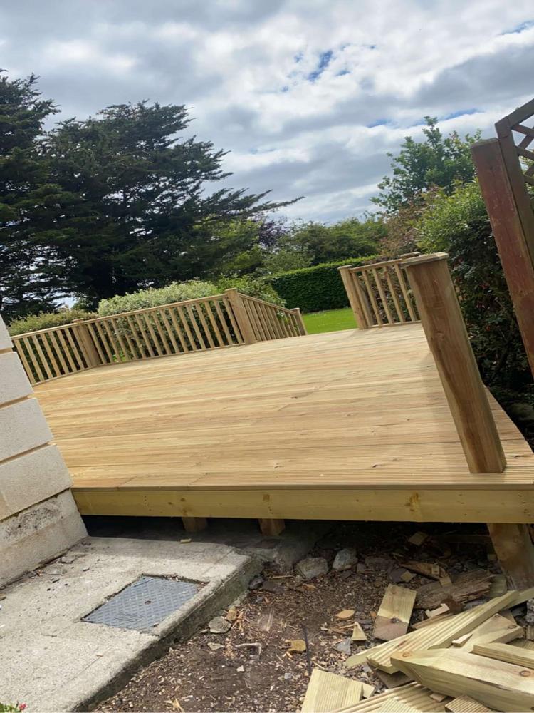 Newly constructed wooden deck with railing made from natural timber, showcasing craftsmanship and wood quality against a backdrop of trees and cloudy sky.