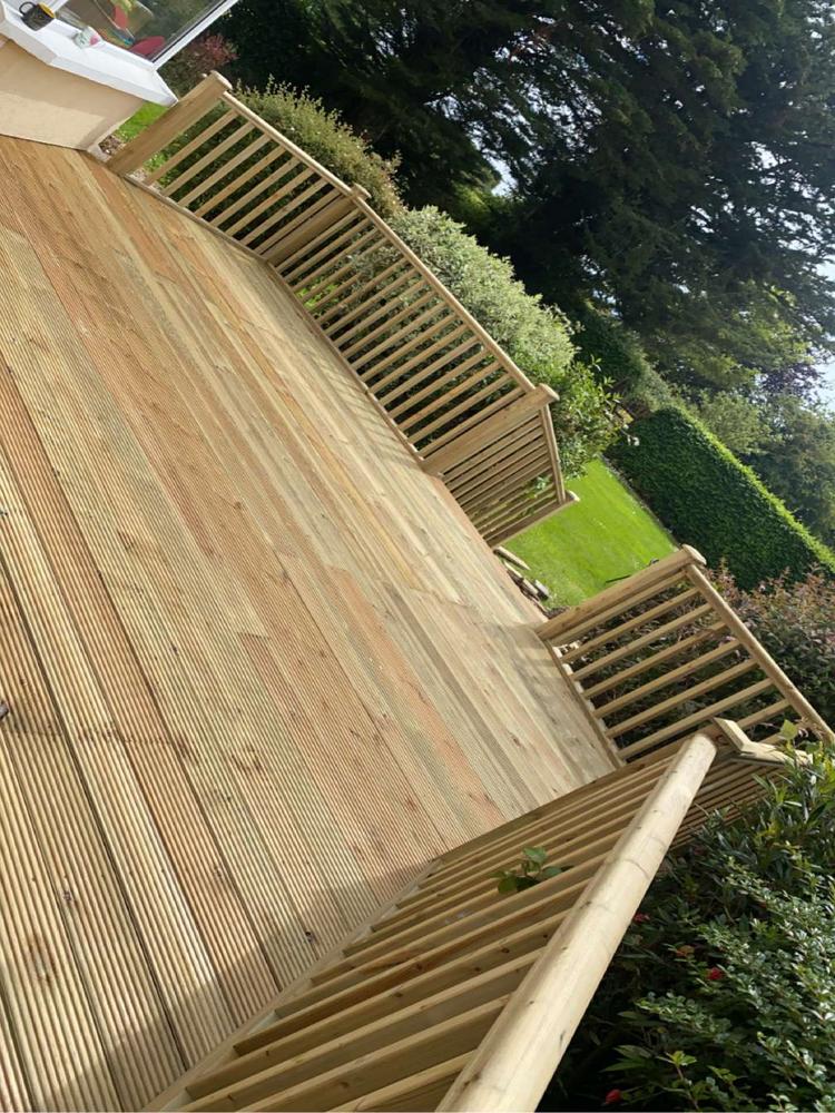 Elevated wooden deck with grooved timber floorboards and matching railings, showcasing the natural beauty and craftsmanship of wood, surrounded by lush greenery.