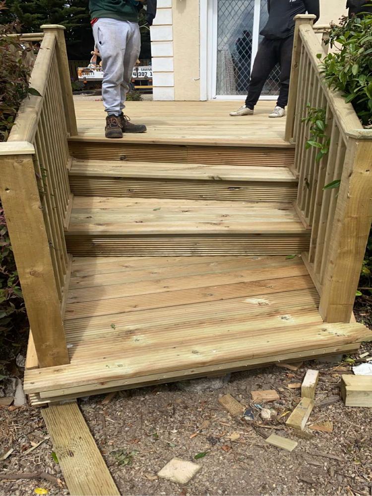 Wooden staircase constructed with high-quality timber, showcasing craftsmanship suitable for sawmilling, bespoke table designs, and intricately carved wood, with two individuals standing on the finished structure, illustrating the timber company's proficiency and attention to detail in woodwork.